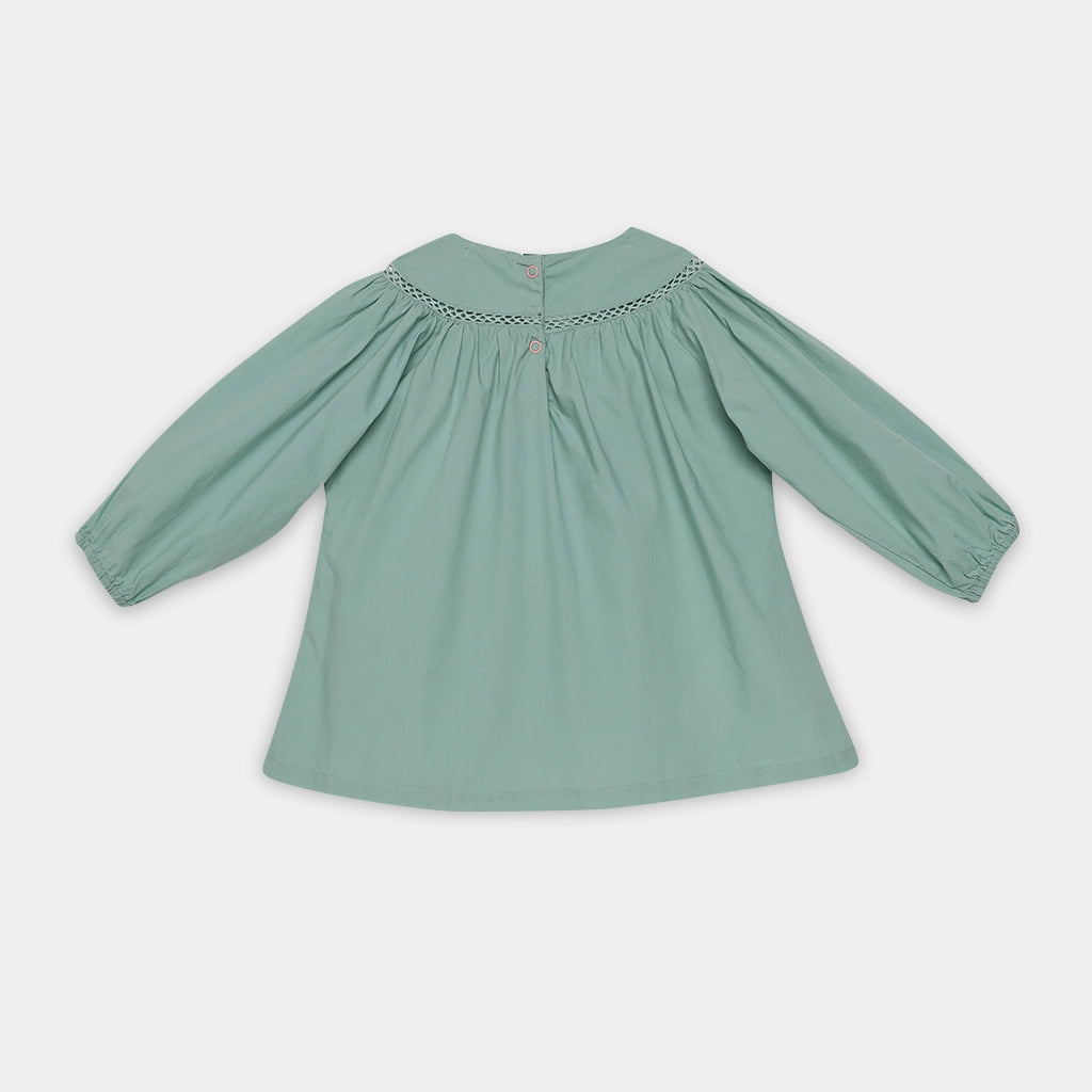 Green blouse with smocked neckline on a light gray background