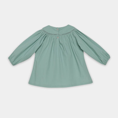 Green blouse with smocked neckline on a light gray background