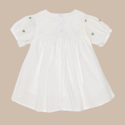 White baby dress with green heart details on a white background