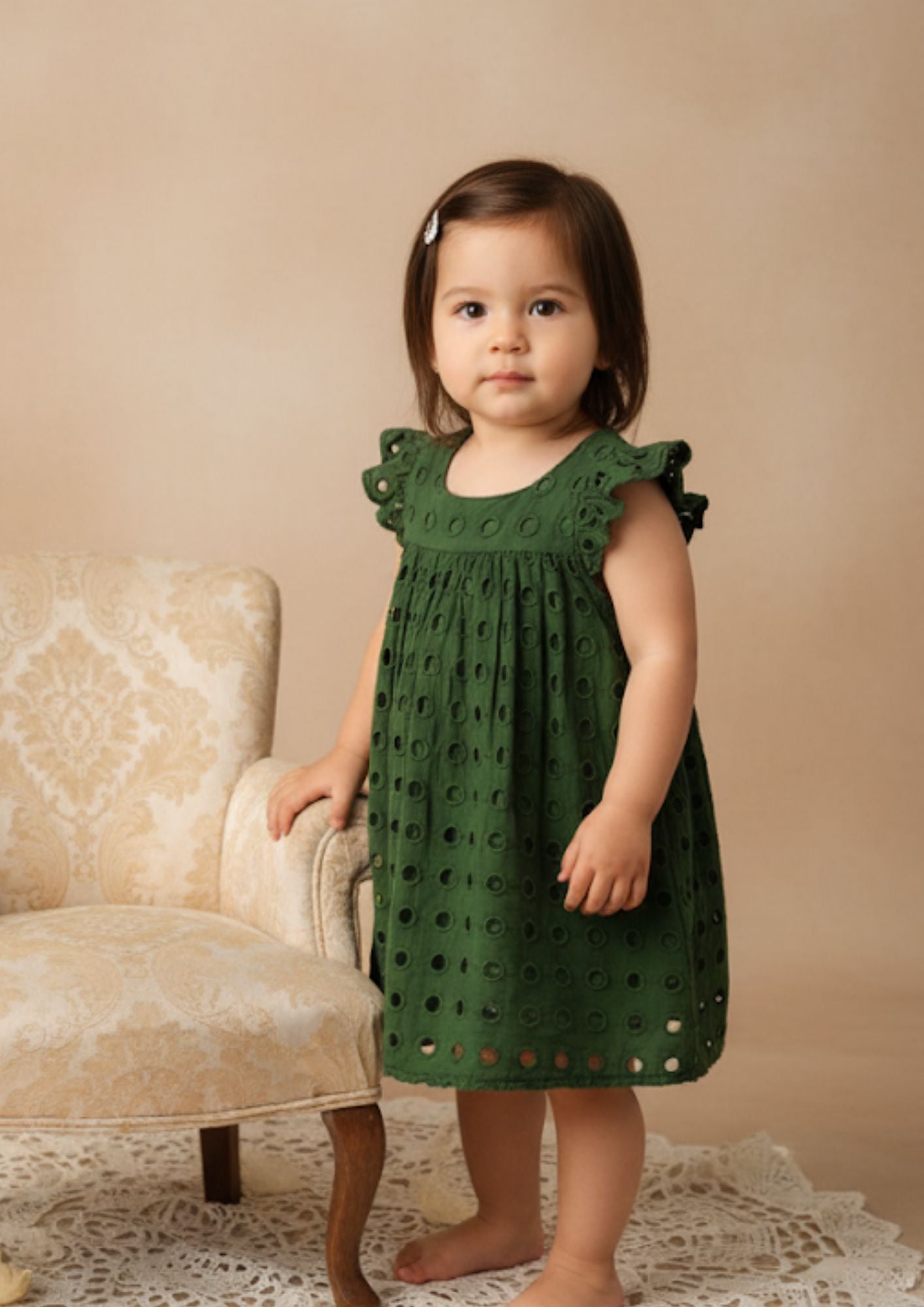 Baby girl standing with hand on chair wearing green hakoba cotton A-line dress