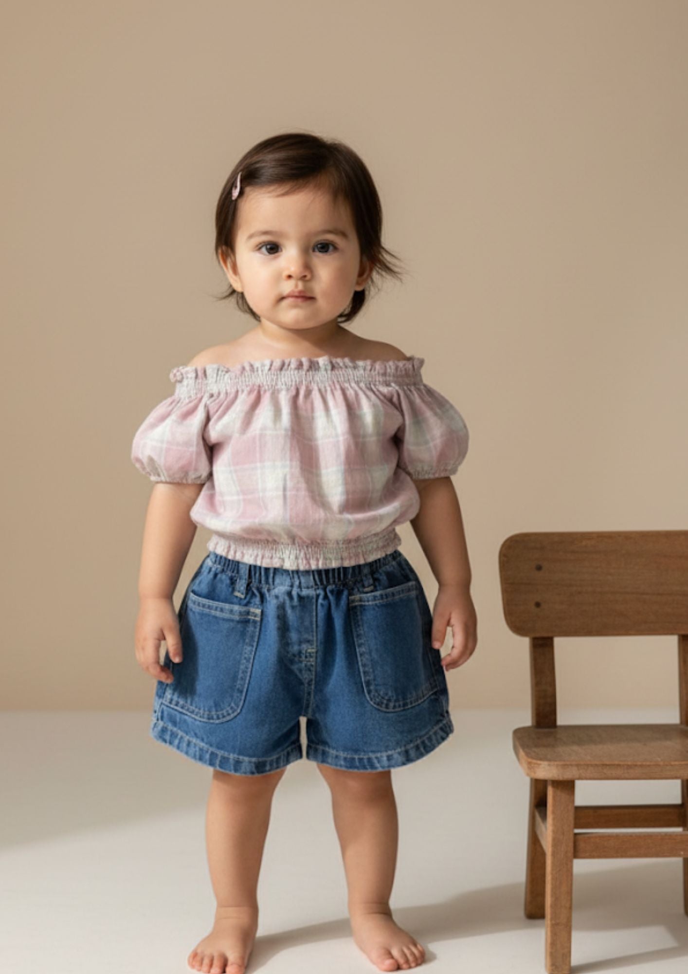 Baby girl standing wearing pink checked drop shoulder crop top and dark blue denim shorts