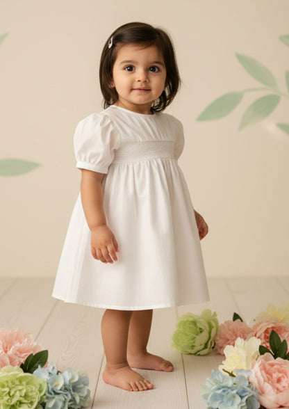 Baby girl standing sideways wearing pure white smocked cotton A-line dress