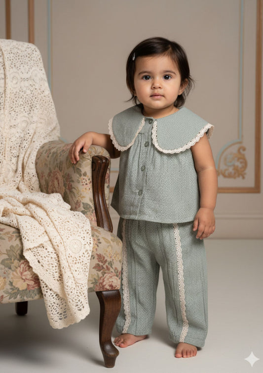 Baby girl standing with hand on chair wearing sage green tiny checks cotton co-ord set with Peter Pan collar