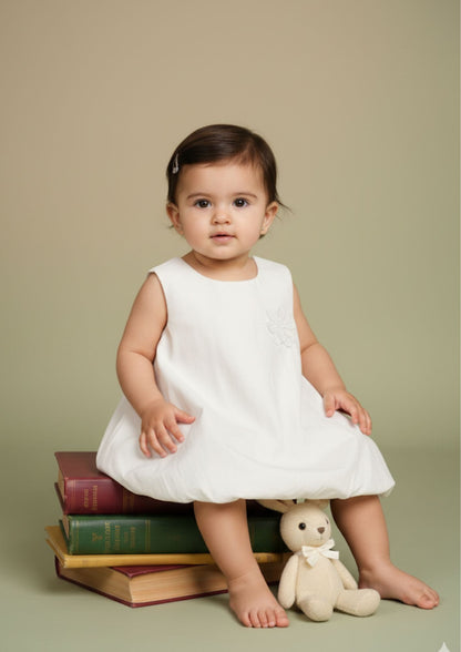 Baby girl sitting on books wearing white balloon-fit cotton dress